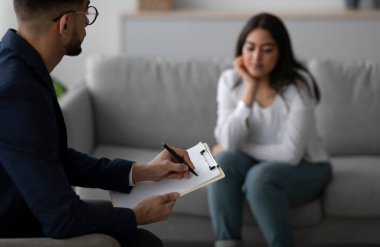 Sessiz bir terapi ofisinde, genç bir Arap kadın düşüncelerini düşünürken erkek bir psikolog panoya yazı yazar. Atmosfer odaklı ve destekleyici..