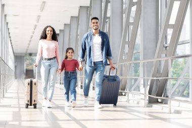 Üç kişilik bir aile geniş bir havaalanı terminalinde el ele yürüyor. Yaklaşan yolculuklarına hazırlanırken mutlu ve heyecanlı görünüyorlar. Yanında bavullarıyla..