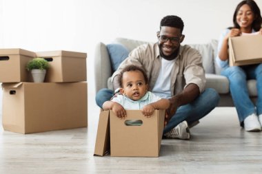 Parlak yeni bir dairede, neşeli siyah bir aile taşınma gününü kutluyor. Gözlüklü bir baba, küçük oğlunu karton bir kutuya bindirip oturma odasında eğlenceli bir ortam yaratıyor..