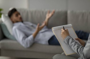 Sakinleştirici bir muayenehanede bir psikolog, orta doğulu bir erkek hasta kanepede uzanmış, stres ve depresyon hislerini dile getirirken notlar alır..