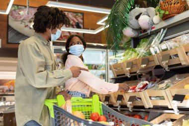 İki kişi bir markette birlikte alışveriş yapıyor, maske takıyor. Onlar sohbet ederken taze sebze ve meyve seçiyorlar..
