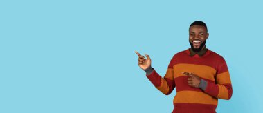 Look There. Smiling black man pointing aside at copy space on blue background with two hands, handsome young african american male demonstrating free place for your advertisement or design, panorama