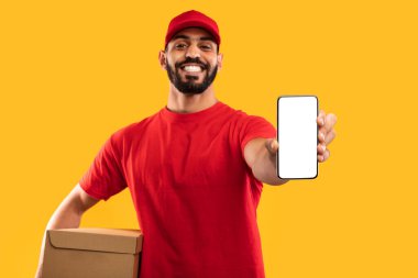 Kırmızı gömlekli ve şapkalı bir teslimatçı bir elinde akıllı telefon, diğer elinde karton kutu tutarken gülümsüyor. Parlak sarı arka plan neşeli sahneyi vurgular.