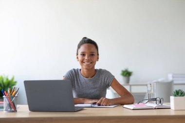 Tatmin olmuş bir Afro Amerikalı kız öğrenci evdeki masasında oturuyor. Not alırken online dersini bir dizüstü bilgisayardan alıyor. Mekan parlak ve davetkar. Öğrenmek için mükemmel..