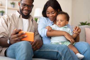Afro-Amerikan ailesi evde kanepede kaliteli zaman geçirmeyi sever. Ebeveynler akıllı telefonu erkek çocuklarıyla paylaşıyorlar, fotoğraf gösteriyorlar ve bir video görüşmesi sırasında dedeleriyle iletişim kuruyorlar..