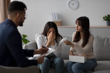 Terapi seansında, bir ortadoğulu kadın partneri onu rahatlatırken ağlıyor. Bir danışman duygularını destekleyici bir ortamda yönlendirirken dikkatle dinler..