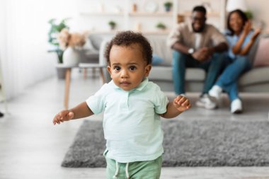 Bebekler keyifli bir şekilde ilk adımlarını salonda atar. Ailesi bu özel anı kutlamak için onu kanepeden kaldırıyor. Atmosfer sevgi ve heyecanla dolu..