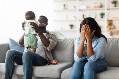 Yorgun bir Afrikalı Amerikalı anne kanepede oturur, stres yüzünden yüzünü gözyaşlarına boğar..