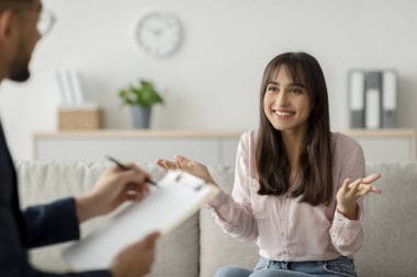 Mutlu Arap kadın terapi sürecini psikoloğuyla paylaşıyor. Seans, psikoterapinin onun sağlığı üzerindeki olumlu etkilerini vurgulayan parlak bir klinik ortamında gerçekleşiyor..