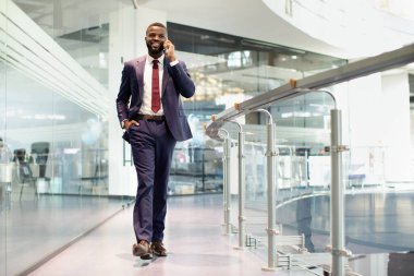 Pahalı mavi takım elbiseli yakışıklı genç bir yönetici modern iş merkezinin önünden geçiyor, iş ortağıyla telefon görüşmesi yapıyor, fotokopi alanı olan bir panorama, tam boy çekim yapıyor.