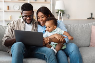 Ebeveynler, dizüstü bilgisayar kullanırken genç oğullarıyla keyifli bir anı paylaşıyorlar. Rahat bir şekilde oturma odasındaki kanepede oturuyorlar, eğlenceli bir aktiviteyle meşguller..