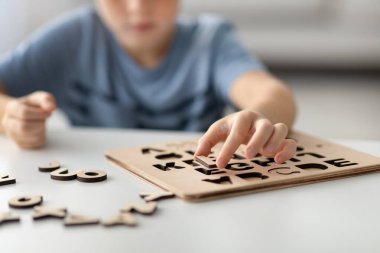 Anaokulundan bir çocuk alfabe harflerinin yer aldığı ahşap bir eğitim oyunuyla evde tek başına oynuyor. Öğrenme faaliyetinin bir parçası olarak mektupları toplamaya odaklanmış..