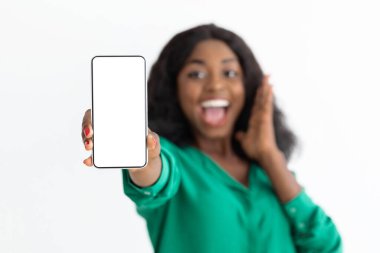 Yeşil bluzlu neşeli bir kadın boş bir akıllı telefon ekranı tutuyor. Bir eli heyecanla yüzüne dönük bir şekilde gülümsüyor. Arka plan parlak ve tarafsız..