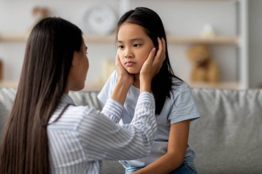 Sıcak bir oturma odasında, genç bir anne anlaşmazlıktan sonra üzgün kızını nazikçe sakinleştirir. Birlikte oturup çocukluk duygularının altını çizerek empati ve anlayış anlarını paylaşıyorlar..