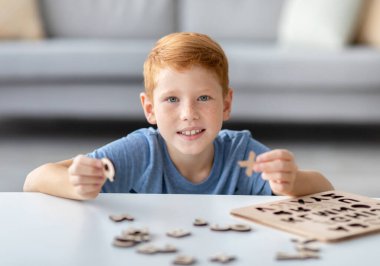Neşeli kızıl saçlı bir çocuk evde tek başına ahşap bir eğitim oyunuyla oynamaktan hoşlanıyor. Alfabeyi incelerken harf toplamaya odaklanmış..