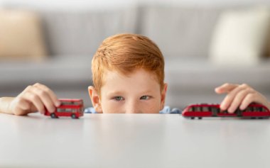 Kızıl saçlı çocuk yeni oyuncak arabaları ve evde tramvayıyla oynuyor. O, tek başına oyun zamanının keyfini çıkarırken odaklanmış ve mutludur, çocukluk eğlencesini keşfeder..