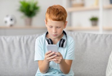 Neşeli bir kızıl çocuk evdeki bir kanepede rahat bir şekilde oturur, akıllı telefonuna odaklanır. Arkadaşlarıyla sohbet etmeyi, oyun oynamayı ve rahat bir atmosferde yeni uygulamalar keşfetmeyi seviyor..