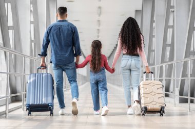 Bir aile geniş bir havaalanı terminalinde el ele yürür, bavullarını taşır. Birlikte maceralarını dört gözle bekliyorlar, neşe ve beklenti gösteriyorlar..