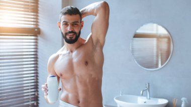 İyi ışıklandırılmış bir banyoda elinde ahşap panjurlarla duran bir adam. Kendine güvenen bir ifadesi var, ve ortam sakin ve şık, çağdaş bir tasarım sergiliyor..