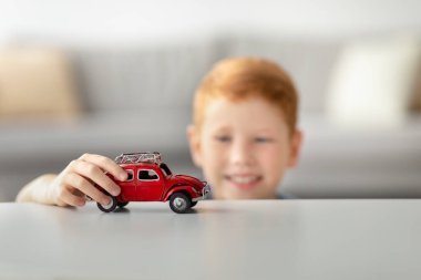Kızıl saçlı tatlı bir çocuk beyaz bir masada kırmızı bir araba oyuncağıyla oynamaktan hoşlanıyor. Küçük bir klasik otomobil kullanıyor, evde yaratıcı oyunlarla mutlu mesut meşgul..