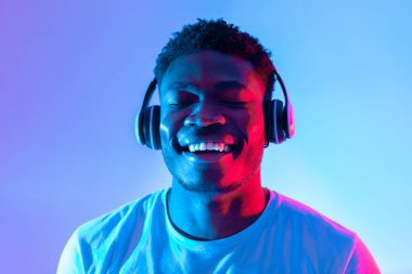 Genç bir adam kulaklıkla müzik dinlerken geniş ölçüde gülümser. Işık, o anın neşesini arttırmak için mavi ve pembe tonlarıyla canlı bir atmosfer yaratıyor..