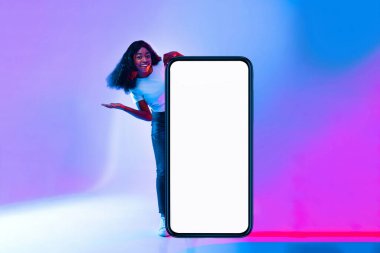 Neşeli genç bir kadın büyük boş bir akıllı telefon ekranının yanında duruyor ve dikkat çekiyor. Renkli arka plan pembe ve mavinin tonlarına sahip, canlı bir atmosfer yaratıyor..