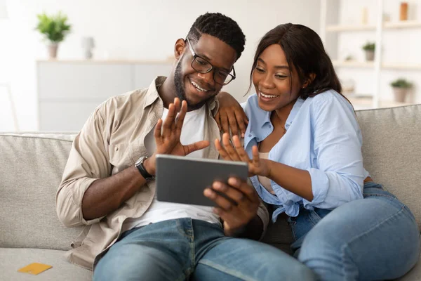 Gülümseyen bir çift rahat bir oturma odasında kanepelerinden eğlenceli bir video görüşmesi yapıyor. Arkadaşlarıyla ya da aileleriyle iletişim kurmak için tablet kullanırken el sallarlar ve gülümserler..