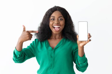 Kıvırcık saçlı neşeli bir kadın diğer elinde tuttuğu akıllı telefonu heyecanlı bir şekilde işaret eden beyaz bir duvara dayanıyor. Coşkuyla gülümsüyor..