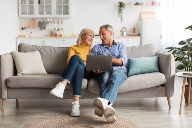 İki gülümseyen yetişkin rahat bir koltukta dizüstü bilgisayarla meşgul oluyorlar. Sıcak etkileşimleri ve rahat çevreleri evlerinde neşeli bir atmosfer yaratıyor..