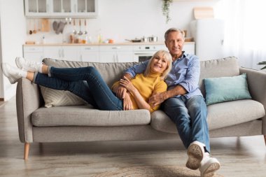 Mutlu bir çift, parlak bir mutfakta rahat bir kanepede birlikte vakit geçirmekten zevk alır. Rahatlarken gülümserler, birbirlerini kucaklarlar bir neşe ve bağ anında..