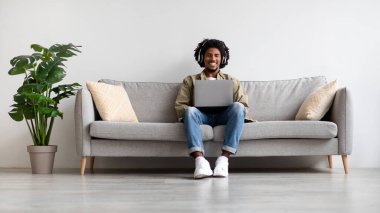 Neşeli bir Afro-Amerikalı adam evinde kablosuz kulaklık takıyor ve dizüstü bilgisayarında internette geziniyor. Etrafı yeşilliklerle çevrili bir kanepede rahatça oturur ve zamanının tadını çıkarır..