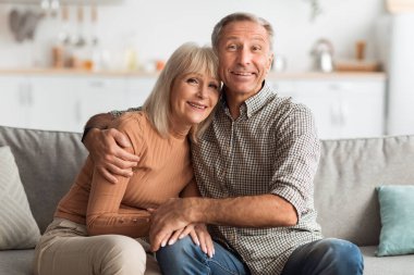 Mutlu yaşlı bir çift, parlak oturma odalarındaki rahat bir kanepede yan yana oturur. Rahatlamış bir öğleden sonra birbirlerine eşlik ederek kameraya sıcak bir şekilde gülümserler..