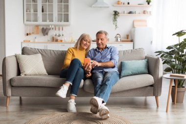 Aydınlık ve davetkar bir oturma odasında, bir çift bir koltukta yan yana oturur, akıllı telefona bakarken paylaşılan anın tadını çıkarırlar. İfadeleri sıcak ve neşeli..