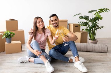 Genç bir çift yeni oturma odalarının zemininde oturuyor, etrafı kutular ve bitkilerle çevrili. Şampanya kadehleriyle kadeh kaldırırlar. Yeni hayatlarına başlarken mutlu bir şekilde gülümserler..