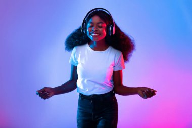 Bir kadın kulaklık takarken neşeli bir gülümsemeyle ayakta duruyor. Müzikte kaybolmuş ve canlı mavi ve pembe ışıklarla çevrelenmiş. Kaygısız ruhu o anda ışıldıyor..