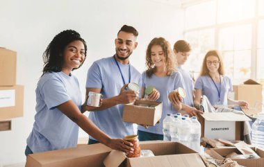Gülümseyen gönüllülerden oluşan gruplar, ihtiyacı olan ailelere yiyecek dağıtımı için parlak bir toplum merkezinde birlikte çalışıyorlar. Arkadaşlıkları fedakârlık ruhunu ön plana çıkarıyor..