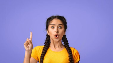 Koyu renk örgülü genç bir kız şaşkınlığını ifade eder, ağzı huşu içinde açıktır. Canlı bir mor arka plana karşı duruyor, bir parmağını kaldırıyor, sanki bir düşünceyi ya da keşfi paylaşıyormuş gibi..