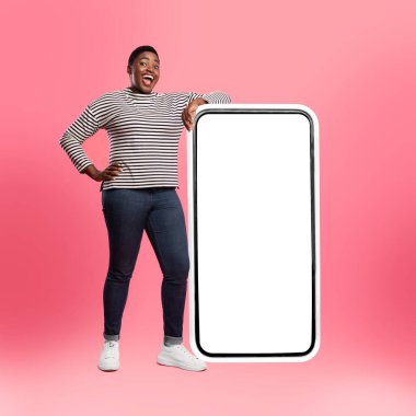 Bir insan canlı pembe bir arka planda boş bir akıllı telefon ekranının yanında güvenle durur. Büyük gülümsemeleri ve canlı duruşları teknolojiyle olan bağlarını ve mutluluklarını gösteriyor..