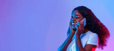 Kıvırcık saçlı genç bir kadın cep telefonuyla mutlu bir şekilde konuşuyor. Parlak bir şekilde gülümsüyor. Etrafı mavi ve pembe ışıklarla çevrili..