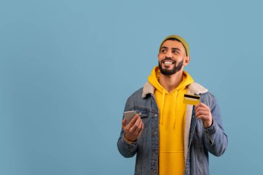 Bir adam neşeyle bir elinde kredi kartı, diğer elinde akıllı telefon tutuyor..