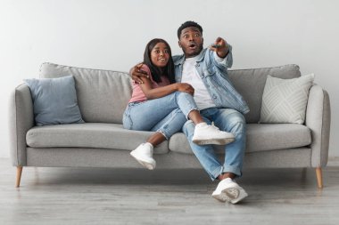 Vay canına Omg. Heyecanlı bir Afro-Amerikan çiftin portresi televizyon programı ya da film izlerken ağzı açık kanepede oturup sarılıyor. Şok olmuş adam uzaktan kumandayı elinde tutuyor, ailesinin son dakika haberi.