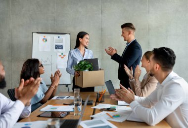 Modern bir ofiste, bir grup iş adamı yeni Asyalı bayan meslektaşlarını alkışlıyor. Bu karşılama anı, bir konferans ortamında takım çalışmasının ve işbirliğinin altını çiziyor.