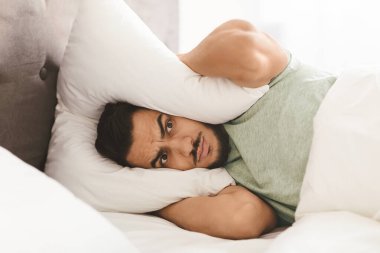 Genç bir adam yatağında, kulağına yastıklar tutarak gürültüyü engelliyor. Hüsrana uğramış ve uykusuz görünüyor. Etrafı yumuşak yataklarla çevrili..