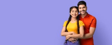 Genç bir çift birbirine yakın duruyor, kameraya samimi bir şekilde gülümsüyor. Arka plan parlak bir mor, neşeli ifadelerini geliştiriyor. Rahat ve dost canlısı görünüyorlar..