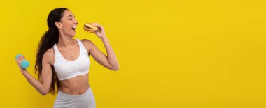 Bir kadın bir elinde dambıl diğer elinde hamburger tutarak eğleniyor. Canlı sarı bir arka planda hem zindelik hem de hoşgörüyü kucaklarken neşe gösteriyor..