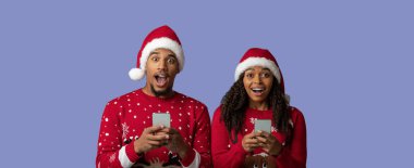 Noel süveteri ve Noel Baba şapkası giyen neşeli bir çift akıllı telefonlarına bakarken heyecanlı bir anı paylaşıyor..