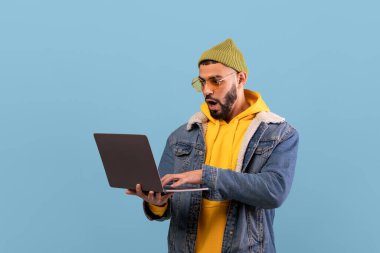 Şık bir kot ceket ve sarı kapüşonlu genç bir adam dikkatle dizüstü bilgisayara bakıyor. Yüzündeki ifade şaşkınlık ya da heyecan gösteriyor, muhtemelen gördüklerinden dolayı..