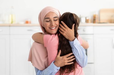 Sıcak bir mutfakta, iki kadın samimi bir kucaklaşmayı paylaşıyor, neşe ve sıcaklık saçıyor. Sahne onların derin bağlarını ve duygusal bağlantılarını vurguluyor, sakin bir ev ortamıyla çevrili..