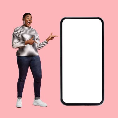 Neşeli bir birey boş bir akıllı telefon ekranının yanında duruyor, gülümsüyor ve heyecanla işaret ediyor. Arkaplan canlı bir pembe renk içeriyor, canlı atmosfere ekliyor..