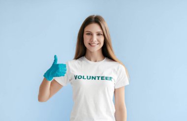 Uzun saçlı genç bir kadın mavi bir arka planda duruyor. 